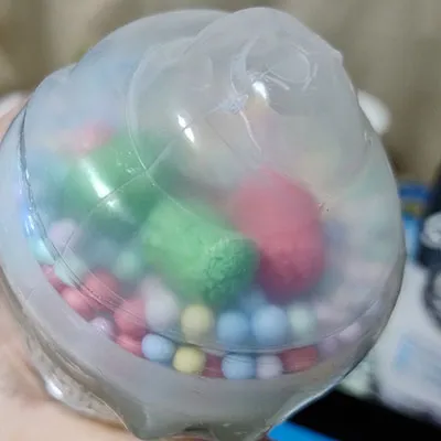 Slime jaune avec de petites boules colorées et trois rouleaux colorés plus grands dans le couvercle en plastique du jouet.