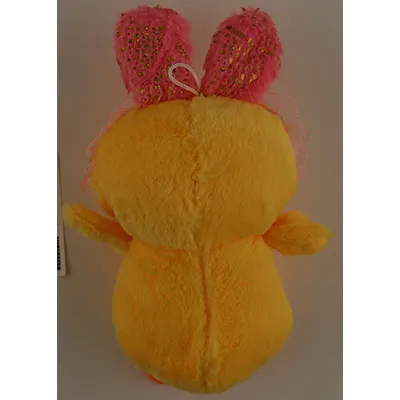 Jouet en peluche, en forme de canard jaune, avec des oreilles de lapin roses, des pieds palmés orange, des yeux en plastique noir et un bec en plastique orange. Une boucle blanche est attachée à la tête du jouet.