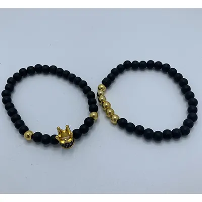 Paire de bracelets avec des perles noires en métal peint et des perles en plastique de couleur or. Un charme de couronne en métal orne l'un des bracelets.