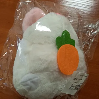Jouet blanc en peluche en forme de lapin avec une carotte, des oreilles roses, des yeux noirs, un anneau de ficelle autorétractable et un accessoire de queue en plastique dur. Lorsque l'anneau de corde auto-rétractable est tiré, le lapin remue sa queue.