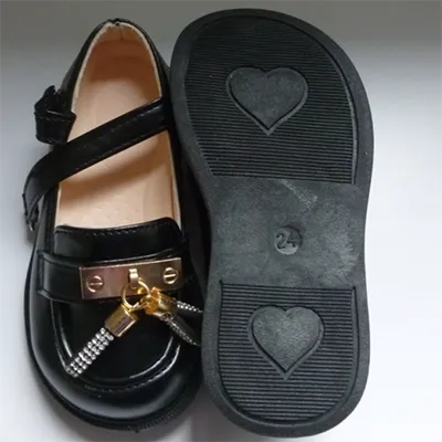 Chaussures pour enfants, de couleur noire, présentant un motif de mocassin avec une sangle de selle, des pompons et une fermeture en velcro. Tailles 21 et 24.