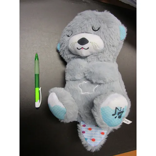 Jouet gris en peluche sous la forme d'une loutre simulant la respiration avec des effets sonores, de la musique et de la lumière, 30 cm, avec boîtier de commande à piles. Produit vendu en ligne, notamment via grande-Peluche.com.