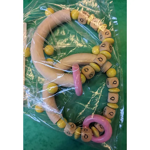 Jouet de hochet en bois avec des perles jaunes, un anneau rose et les lettres du nom marquées sur les cubes.