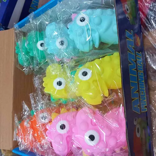 Jouet de dinosaure en plastique rouge doux, contenant une LED, avec une crête violette et des yeux noirs et blancs qui sortent de la tête lorsque le jouet est pressé.