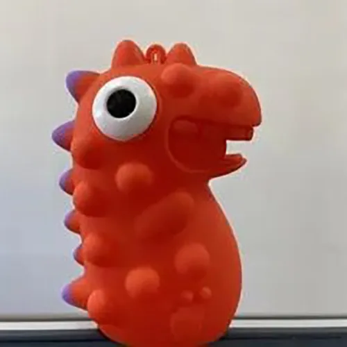Jouet de dinosaure en plastique rouge doux, contenant une LED, avec une crête violette et des yeux noirs et blancs qui sortent de la tête lorsque le jouet est pressé.