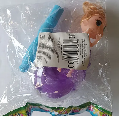 Poupée en plastique dans une robe textile violette. Les pattes de la poupée sont placées dans une boule en plastique transparent avec des plumes. Un contrôleur, y compris une batterie, est fixé à la tête de la poupée.