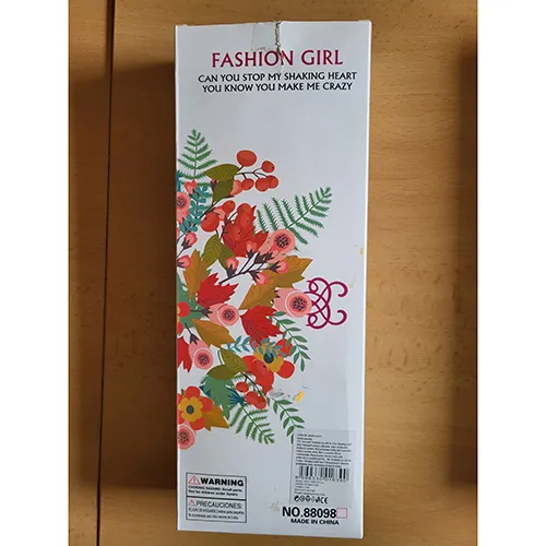 Poupée d'environ 29 cm, avec des accessoires en plastique, des boucles d'oreilles en plastique de couleur argentée sur ses oreilles, de longs cheveux blonds en queue de cheval, vêtue d'une mini robe et des chaussures en plastique rose hautes à semelles et talons hauts.