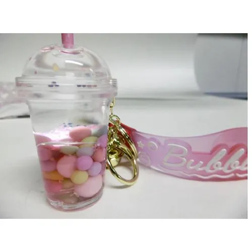 Trois porte-clés avec une figure de tasse à thé à bulles. La figurine en plastique contient deux liquides non mélangeables (roses et transparents) dans des récipients scellés par un bouchon en plastique en caoutchouc. Produit vendu en ligne, notamment via Shein (identifiant produit, SKU: sc2407277808880181).