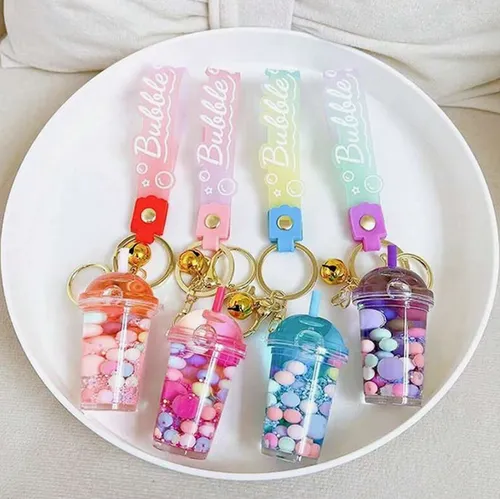 Trois porte-clés avec une figure de tasse à thé à bulles. La figurine en plastique contient deux liquides non mélangeables (roses et transparents) dans des récipients scellés par un bouchon en plastique en caoutchouc. Produit vendu en ligne, notamment via Shein (identifiant produit, SKU: sc2407277808880181).