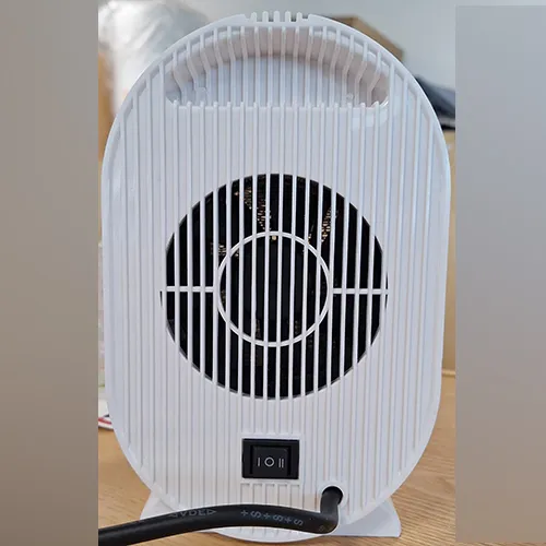 Chauffage de ventilateur blanc de forme ovale avec une grille noire et un cordon d'alimentation noir attaché. Produit vendu en ligne, notamment via Amazon (ASIN: B0CMCZT6QR).
