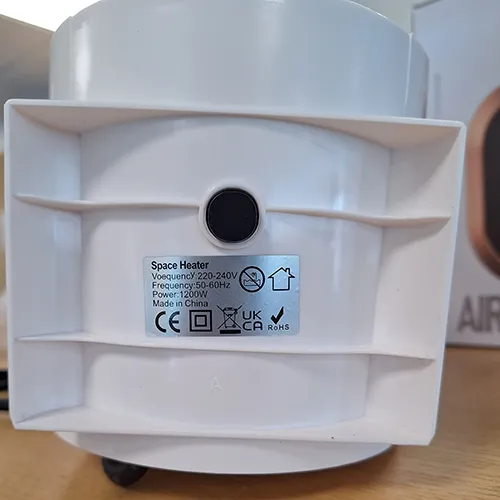 Chauffage de ventilateur blanc de forme ovale avec une grille noire et un cordon d'alimentation noir attaché. Produit vendu en ligne, notamment via Amazon (ASIN: B0CMCZT6QR).