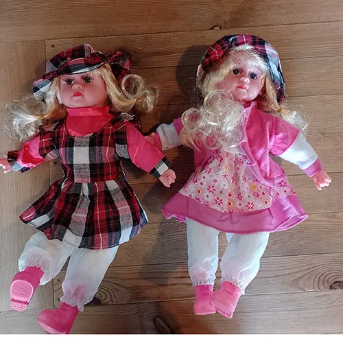 Poupée textile avec une tête, des mains et des chaussures en plastique. La poupée a de longs cheveux blonds et est vêtue d'une robe colorée et d'un caleçon. Sous la robe, il y a un compartiment à piles amovible pour trois pièces de piles LR44.