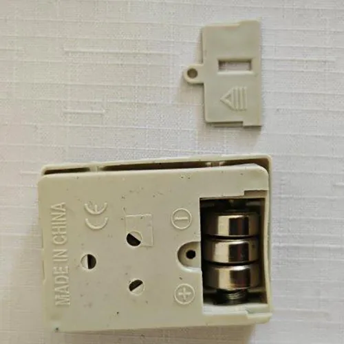 Poupée textile avec une tête, des mains et des chaussures en plastique. La poupée a de longs cheveux blonds et est vêtue d'une robe colorée et d'un caleçon. Sous la robe, il y a un compartiment à piles amovible pour trois pièces de piles LR44.