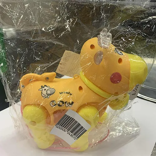 Plastique à piles, a des roues et une ficelle attachée. Le jouet a la forme d'une vache, avec des yeux et des joues peints, des cornes et une cloche transparente attachée au cou.