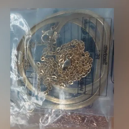 Ensemble de six colliers. Un collier en métal de couleur cuivre avec un charme d'imitation de pierres précieuses. Un collier en métal doré avec un charme de pierre précieuse d'imitation. Une chaîne métallique dorée et simple. Une chaîne à maillons plats dorés. Un collier en métal doré avec un charme de coeur. Produit vendu en ligne, notamment via Temu.