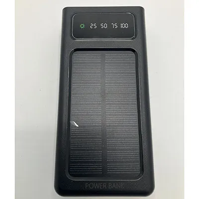 Banque d'alimentation noire, d'environ 25 cm de longueur, avec un panneau solaire, un écran LCD et quatre câbles de chargeur intégrés et deux sorties USB. Produit vendu en ligne, notamment via ovbutiken.se.