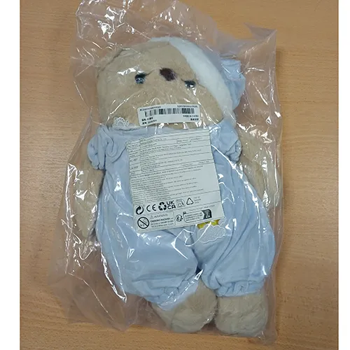 Jouet doux en forme d'ours aux yeux en plastique noir, vêtu d'un pyjama bleu et d'un bonnet de nuit assorti. Produit vendu en ligne, notamment via TikTok.