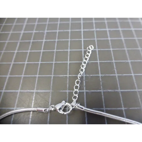 Collier en métal argenté avec pendentifs en métal argenté, noir et doré, fermeture et prolongateur de chaîne.