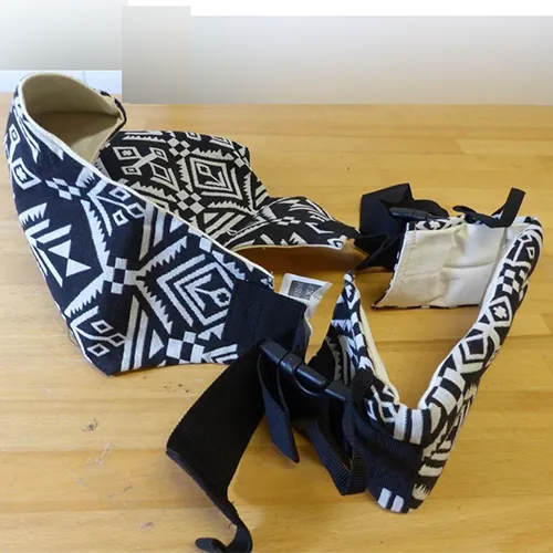 Porte-bébé en tissu blanc avec des motifs noirs et une attache en plastique.