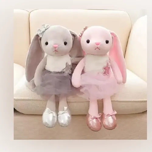 Jouet doux, en forme de lapin rose avec de longues oreilles vertes et roses, portant une robe rose.