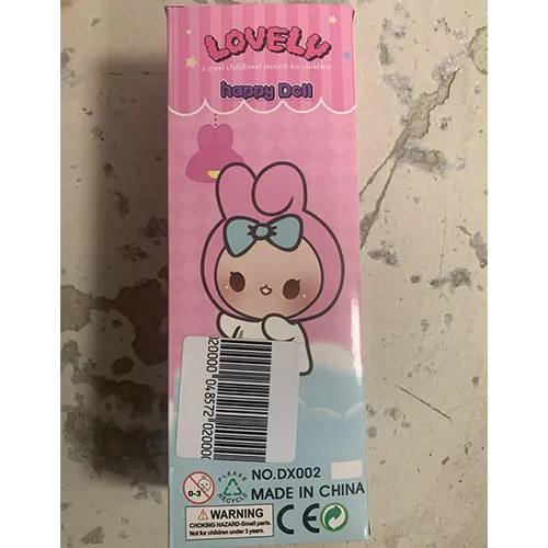 Poupée en plastique, avec des cheveux synthétiques roses, portant un chapeau en textile avec des oreilles décoratives, et habillée de vêtements roses.
