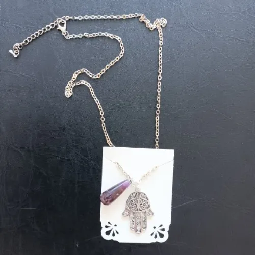 Collier avec deux pendentifs - l'un en métal en forme de main et l'autre est une petite pierre violette en forme de larme.